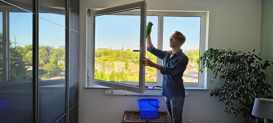 Mann reinigt mit einem grünen Lappen die Fensterrahmen von außen