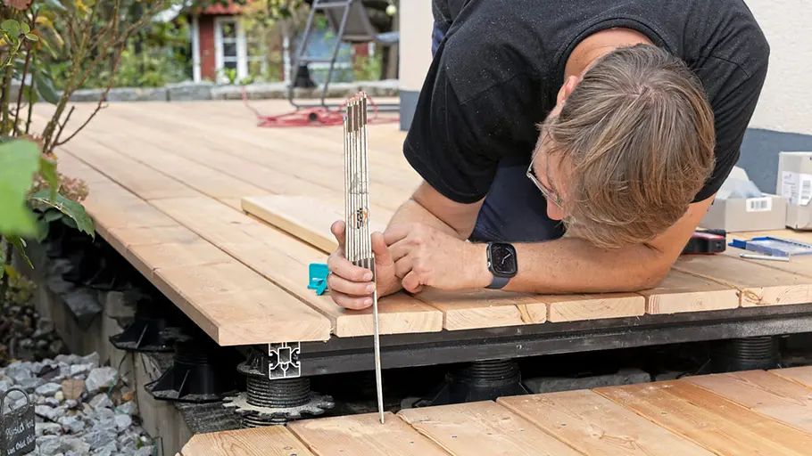 Terrasse gestalten Ein Mann misst mit einem Zollstock den Abstand zwischen zwei Holzterrassenflächen zur Kontrolle der Stufenhöhe.
