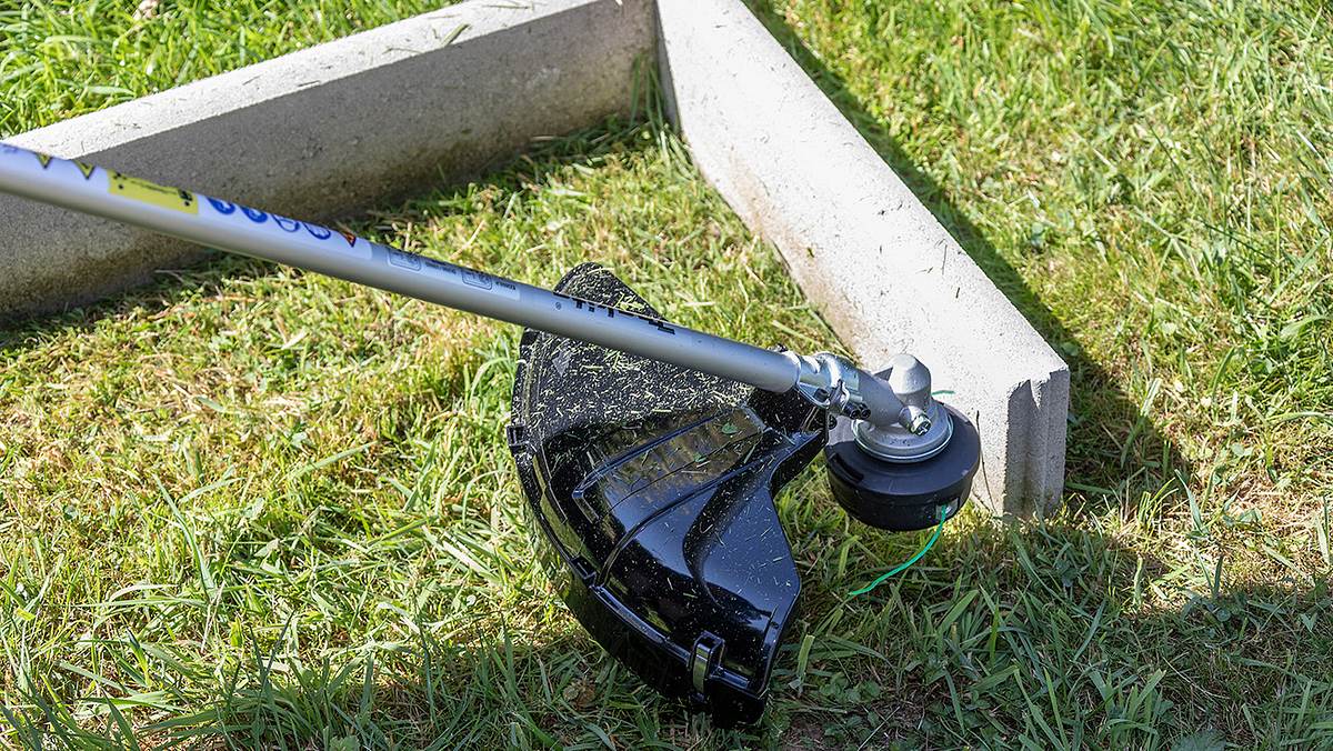 Ein Akku-Rasentrimmer wird an einer Rasenkante aus zwei Betonplatten auf einer Wiese getestet.