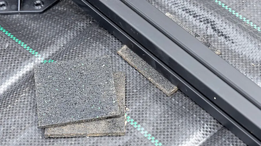 Terrasse gestalten Gummiplättchen liegen neben einer schwarzen Metallunterkonstruktion auf Unkrautvlies und dienen dem Höhenausgleich beim Terrassenbau.