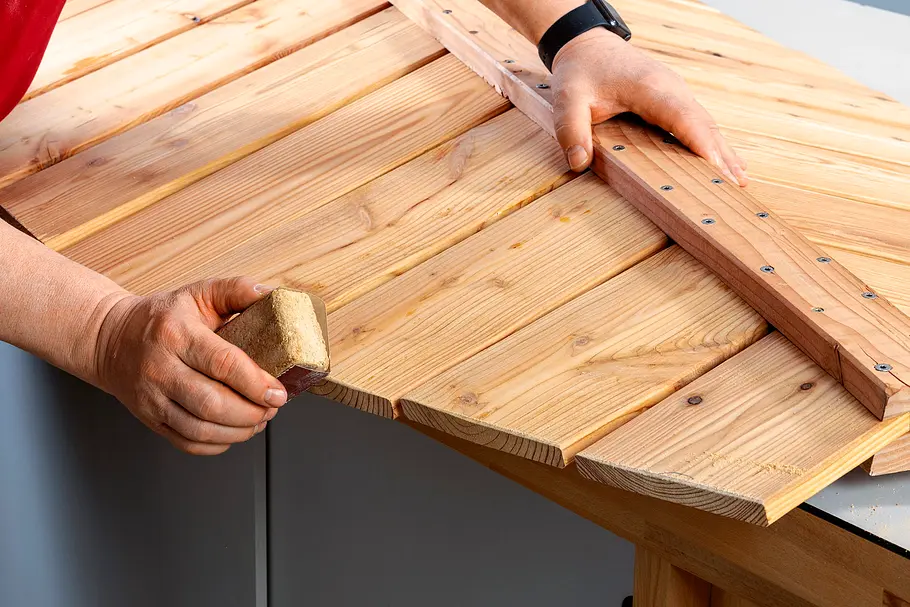 Gartendusche bauen Eine Person richtet die Holzlatten der blattförmigen Konstruktion mit einem Holzhammer aus.