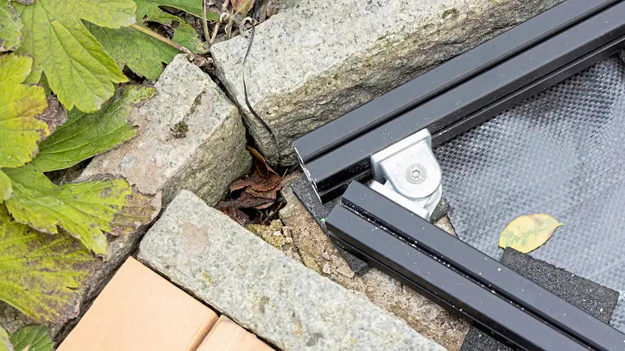 Terrasse gestalten Zwei schwarze Metallprofile der Terrassenunterkonstruktion sind mit einem Winkelverbinder am Rand aus Naturstein befestigt.