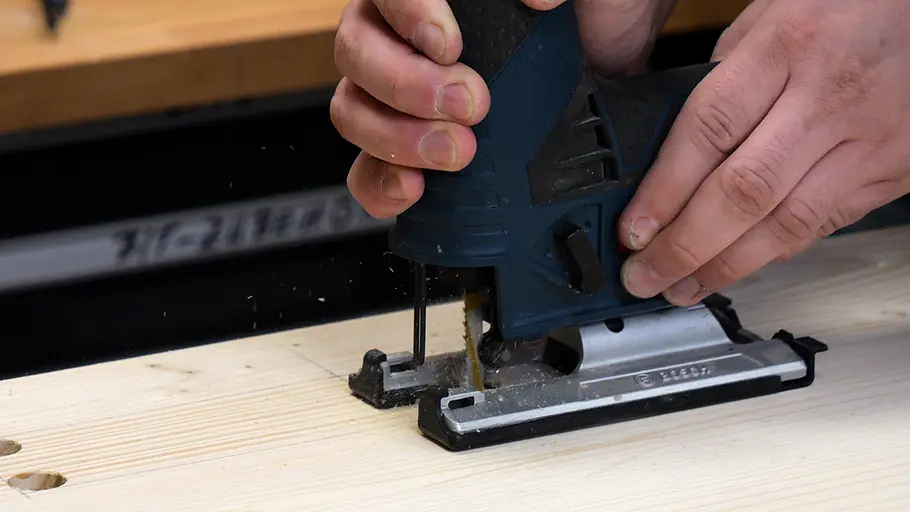 Paketbox Eine Person schneidet eine markierte Linie auf einer Holzplatte mit einer elektrischen Stichsäge aus.