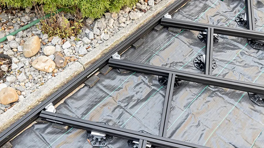 Terrasse gestalten Eine Terrasse erhält eine solide Unterkonstruktion aus diagonal verlegten schwarzen Metallprofilen auf festen Stelzlagern.