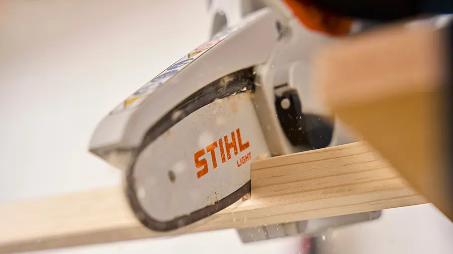 Eine Motorsäge mit STIHL-Logo zersägt ein helles Holzbrett, Holzspäne fliegen beim Sägen durch die Luft.