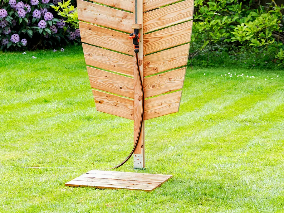 Gartendusche bauen Blattförmige Gartendusche aus Holzlatten mit Kupferrohr und angeschlossenem Gartenschlauch in einem grünen Garten.
