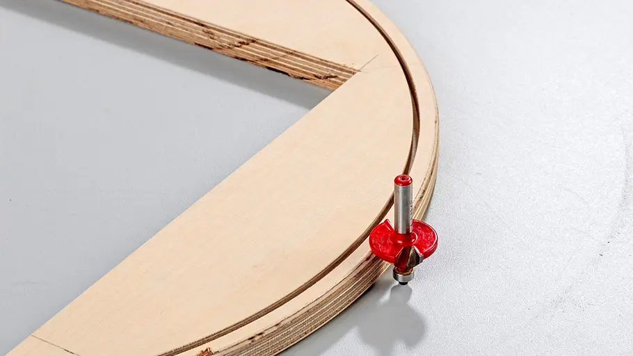 Außenrand fasen Ein rot beschichteter Abrundfräser steht an einem Viertelkreis-Holzrahmen mit sauber gefräster Kante.