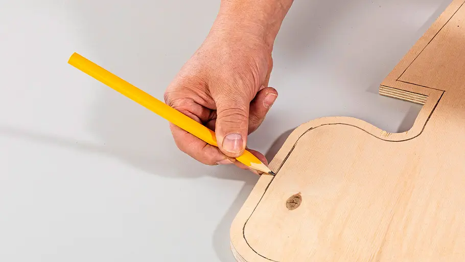 Innenrand aufzeichnen Eine Hand hält einen gelben Bleistift und zeichnet die Konturen einer Kaktusform auf ein Holzbrett nach.