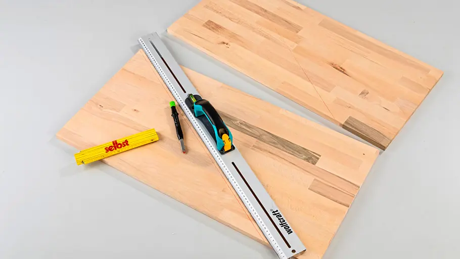 Verdrehter Hocker Zwei Holzplatten mit Lineal, Zollstock und Bleistift liegen auf einer grauen Fläche, Hilfslinien sind eingezeichnet.