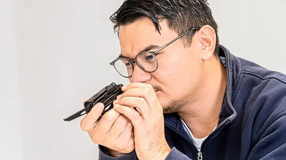Multitool-Test Ein Mann mit Brille betrachtet aufmerksam ein aufgeklapptes Multitool mit sichtbarer Säge in seinen Händen.