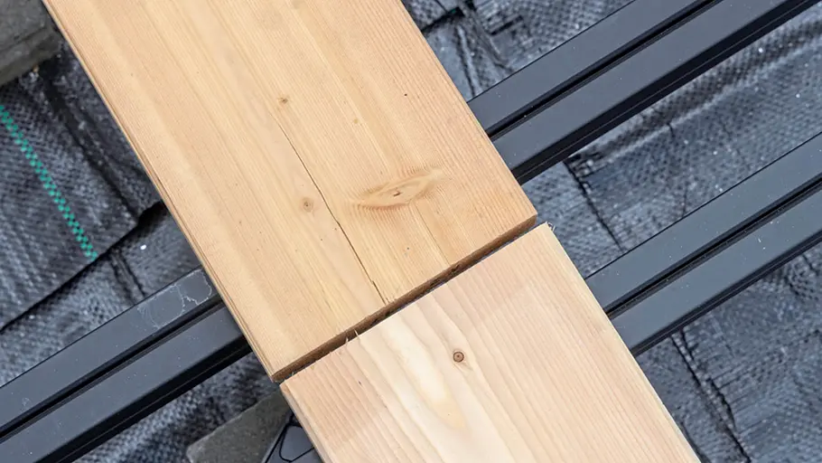 Terrasse gestalten Zwei Terrassendielen mit sauberer Stoßfuge treffen exakt an der schwarzen Metallunterkonstruktion aufeinander.