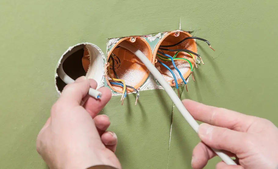 Steckdose anschließen Zwei Hände führen ein Stromkabel durch eine Wandöffnung zu mehreren Hohlwanddosen mit Anschlussdrähten.