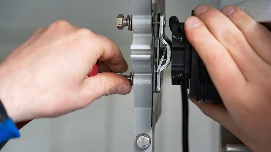 Schrauben kürzen Eine Hand kürzt mit einer Zange die überstehende Schraube an einer Metallhalterung des Markisenmotors.