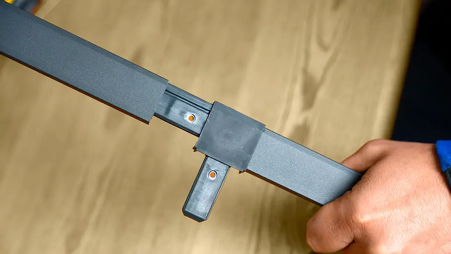 Zwei graue Aluminiumprofile sind über ein schwarzes Kunststoff-T-Verbindungsstück miteinander verbunden.