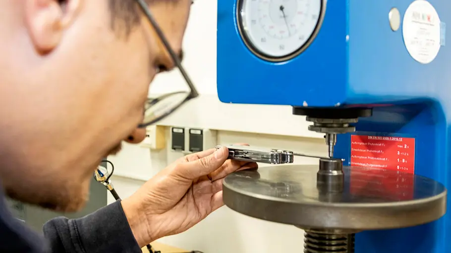 Multitool-Test Ein Mann testet ein Multitool an einer blauen Prüfmaschine mit großem Ziffernblatt in einem Laborraum.