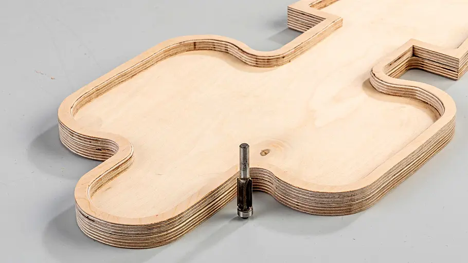 Rand bündig fräsen Ein Fräskopf steht auf einem mehrschichtigen Holzelement in Kaktusform mit abgerundeten Kanten.