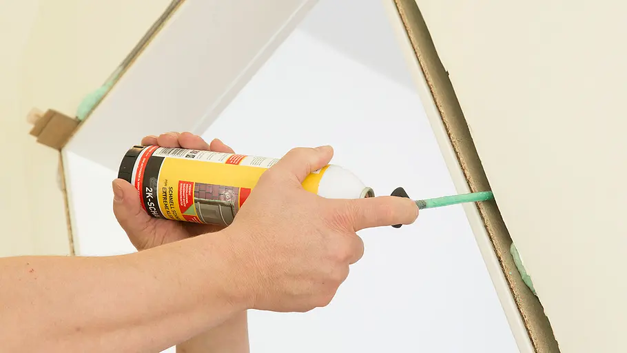 Türschaum verwenden Eine Hand sprüht Bauschaum mit einer Dose in den Spalt zwischen Türrahmen und Wand.