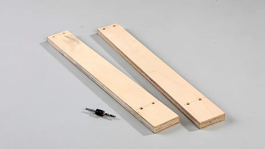 Löcher in Leisten bohren Zwei Holzleisten mit vorgebohrten Löchern liegen parallel nebeneinander, ein Holzbohrer mit Senker liegt davor.