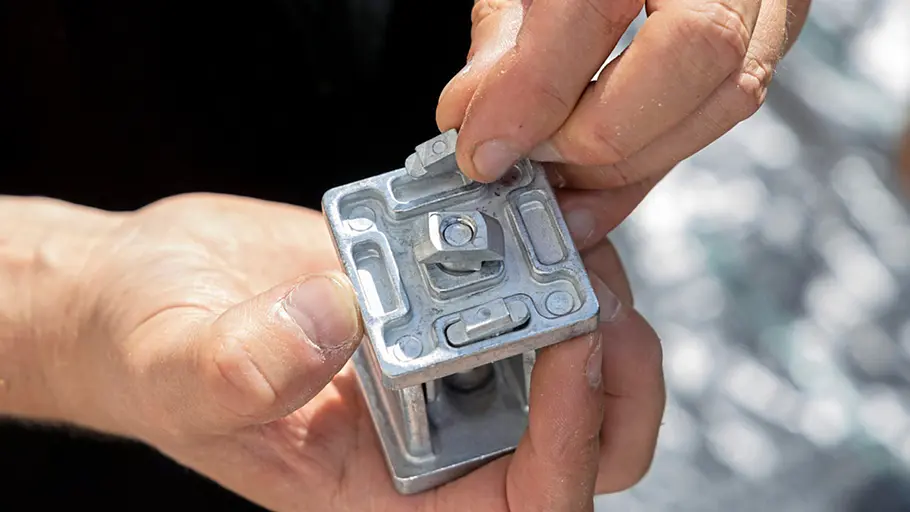Terrasse gestalten Eine Person hält ein Metallverbindungsstück für die Unterkonstruktion der Terrasse und steckt ein kleines Teil ein.