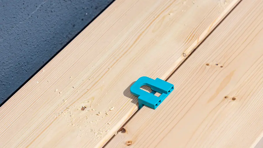 Terrasse gestalten Ein türkisfarbener Abstandhalter befindet sich zwischen zwei nebeneinander liegenden Holzbrettern auf einer Terrasse.