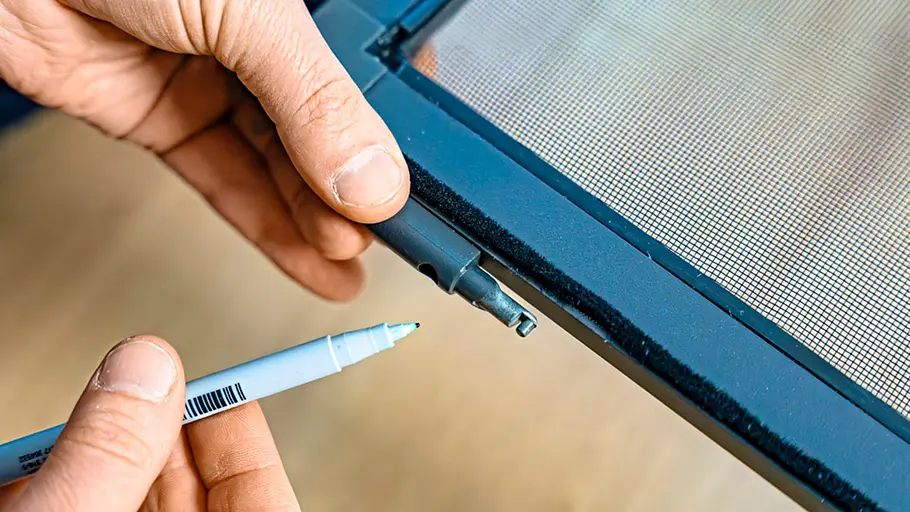 Zwei Hände halten ein rundes Bauteil an den Rahmen der Insektenschutztür, ein Stift markiert eine Position am dunklen Profil.