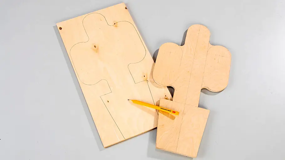 Form aufzeichnen Eine ausgesägte Sperrholzform in Kaktus-Optik liegt neben einer Holzplatte mit aufgezeichnetem Umriss und einem Bleistift.