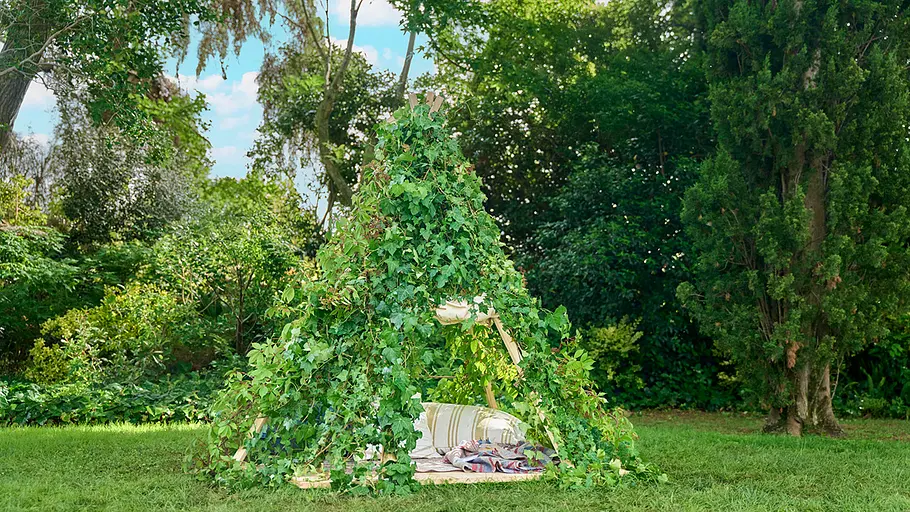 Das fertige Spielzelt ist vollständig mit grünen Kletterpflanzen bedeckt und steht auf einer Wiese im Garten.
