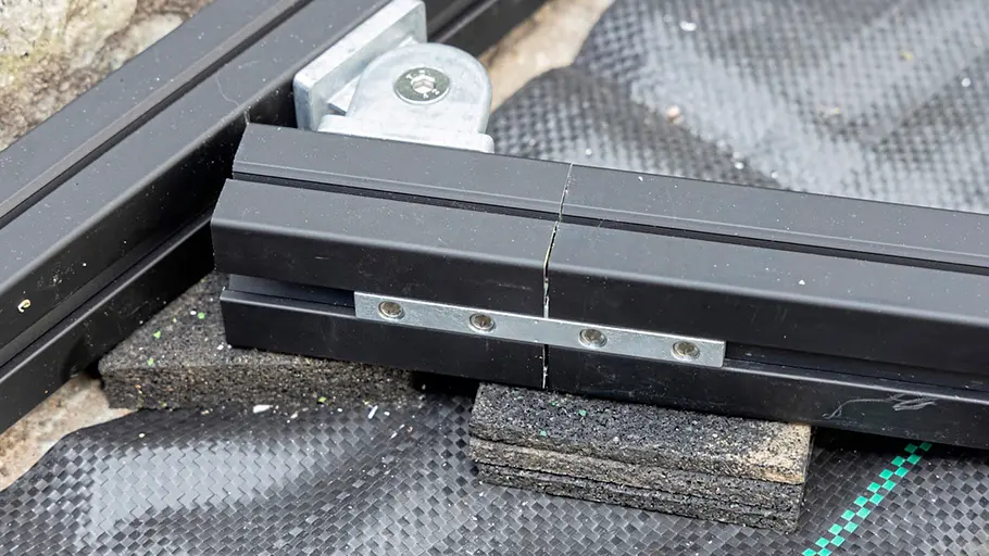 Terrasse gestalten Zwei schwarze Metallprofile werden mit einer Metalllasche verbunden und liegen auf dunklen Gummiplatten auf einem Vlies.