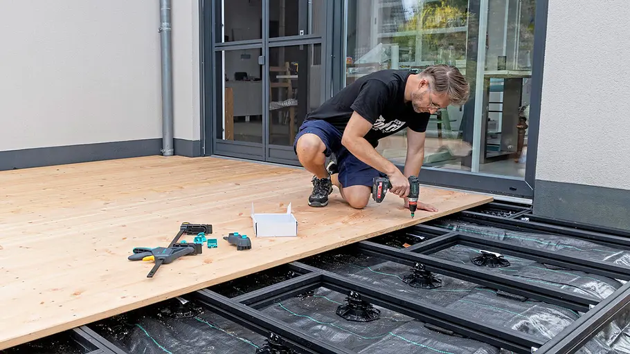 Terrasse gestalten Ein Mann verschraubt Holzdielen auf einer Terrasse, während der Boden Schritt für Schritt fertiggestellt wird.