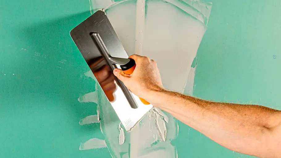 Spachtelmasse Mit einer Glättkelle wird weiße Spachtelmasse auf eine grüne Wand aufgetragen und gleichmäßig verteilt.