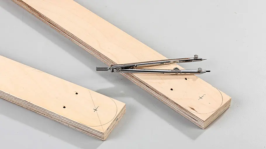 Löcher anbringen Zwei Holzleisten mit angezeichneten Kreisen und Löchern, darauf ein geöffneter Metallzirkel auf grauem Untergrund.