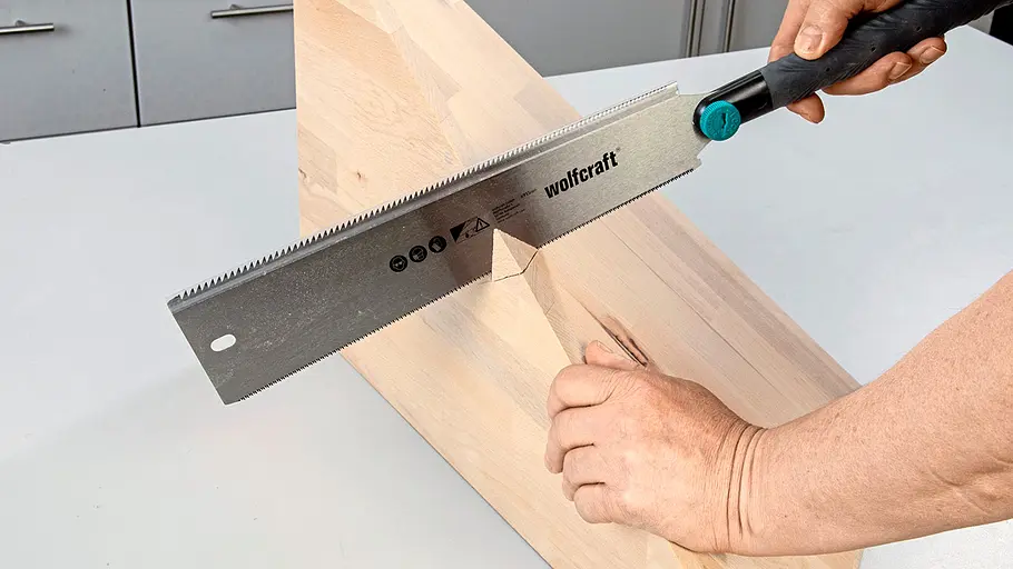 Verdrehter Hocker Eine Person sägt mit einer Handsäge an einem hellen Holzbrett eine schräge Nut für den verdrehten Hocker.