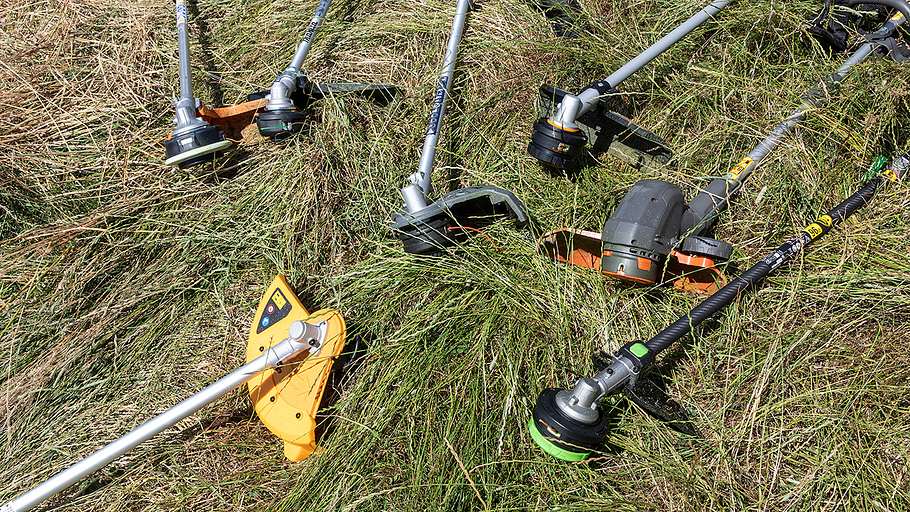 Mehrere Akku-Freischneider verschiedener Hersteller liegen auf einer Wiese mit hohem, geschnittenem Gras.
