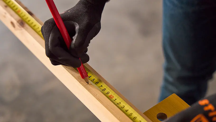 Matschküche: Kanthölzer Eine Person mit schwarzem Handschuh markiert ein Kantholz mit einem Bleistift an einem Maßband bei etwa 55 Zentimetern.