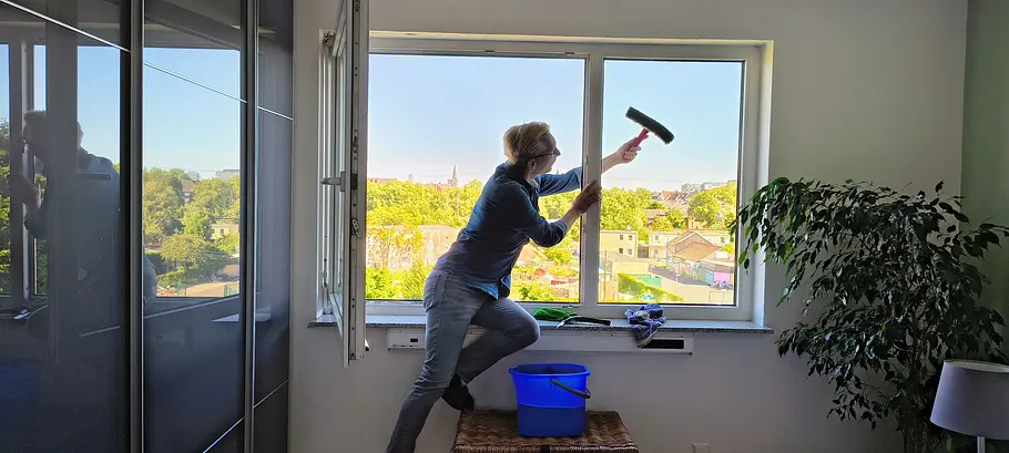 Mann lehnt sich aus dem Fenster, um einen feststehenden Fensterflügel zu reinigen