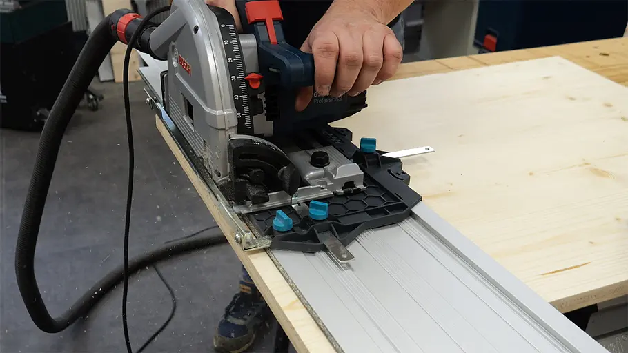 Paketbox Eine Person schneidet mit einer Handkreissäge auf Führungsschiene ein helles Holzbrett an einer Werkbank zu.