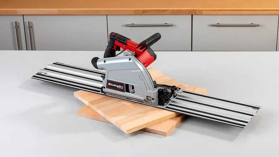 Verdrehter Hocker Eine Handkreissäge mit Führungsschiene liegt auf zwei übereinander gelegten Holzplatten in einer hellen Werkstatt.