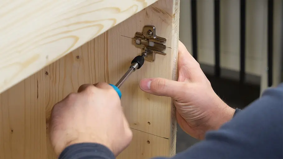 Paketbox Eine Person befestigt mit einem Schraubendreher ein Metallscharnier an der Innenseite einer hölzernen Paketbox.