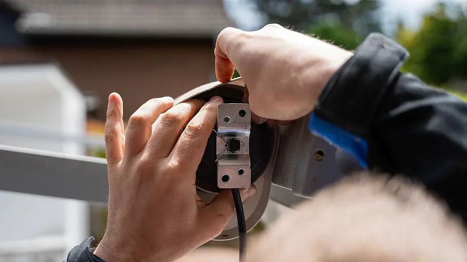 Markisenmotor: Elektrische Leitung Zwei Hände führen die elektrische Leitung des Markisenmotors durch die Halterung und befestigen das Lager mit einer Metallplatte.