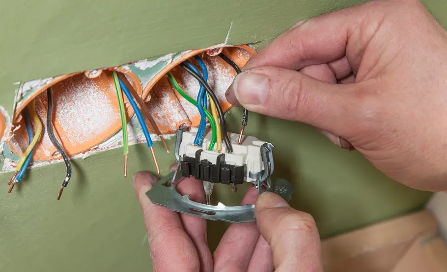Steckdose anschließen Mehradrige Kabel werden an eine Steckdose angeschlossen, Hände halten Steckdose und Kabel.