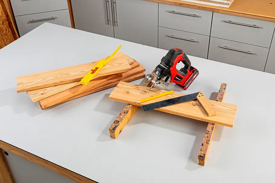 Gartendusche bauen Mehrere zugeschnittene Holzbretter liegen mit Winkel, Zollstock, Bleistift und Handkreissäge auf einer Werkbank.
