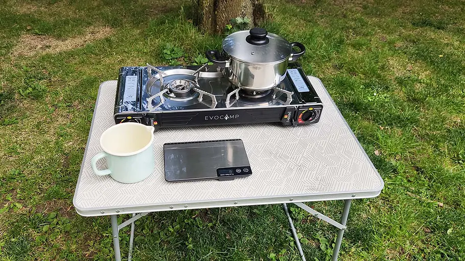 Evocamp Gaskocher 2-flammig Ein zweiflammiger Gaskocher mit Edelstahltopf steht auf einem Tisch, daneben eine Tasse und eine digitale Waage.