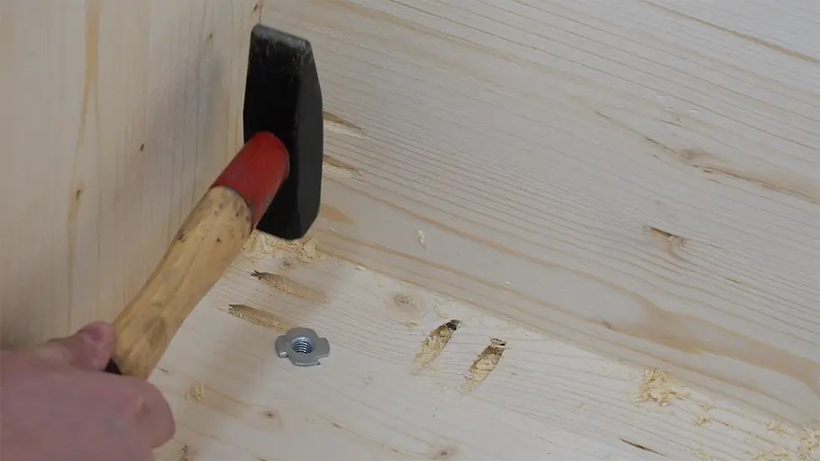Paketbox Eine Hand schlägt mit einem Hammer eine Einschlagmutter in das Holz im Inneren einer hölzernen Paketbox.