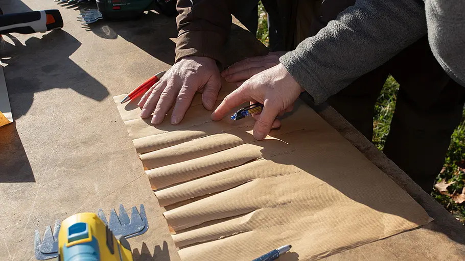 Akku-Grasscheren-Test: Schnitttest Zwei Personen untersuchen auf einem Tisch ein Blatt Papier mit mehreren eingeschnittenen Linien und vergleichen die Schnitte.