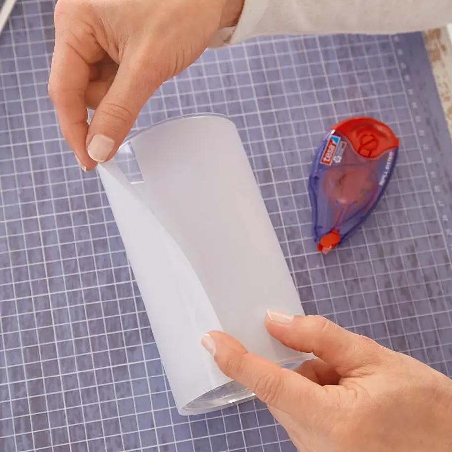 Weihnachts-Windlicht: Funkelndes Sternen-Glas Transparentpapier wird um ein Glas gelegt, während ein Kleberoller danebenliegt.