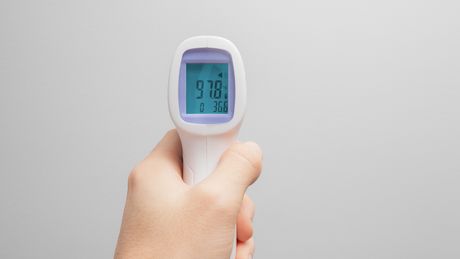 Ein Infrarot-Thermometer wird in der linken Hand gehalten. - Foto: iStock/ frantic00