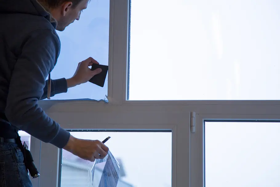 Isolierfolie fürs Fenster: Ein Mann klebt Schutzfolie auf