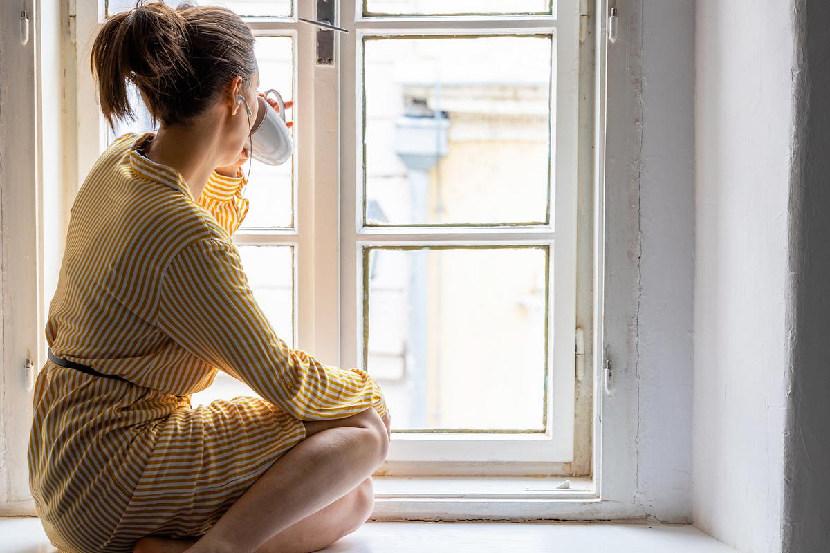 Frau sitzt am Fenster mit Tasse