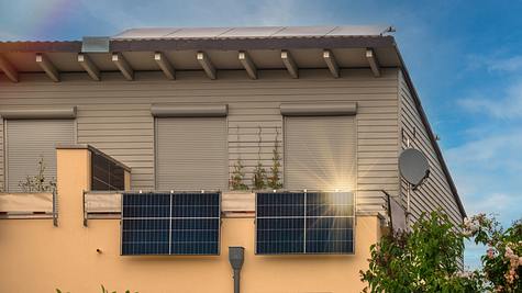 Zwei Balkonkraftwerke hängen am Balkon eines beigen Hauses - Foto: iStock / Frederick Doerschem