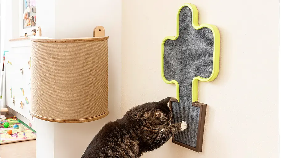 Katzen-Kratzbrett Eine getigerte Katze kratzt mit den Vorderpfoten an einem an der Wand befestigten Kratzbrett in einem hellen Raum.